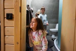 hermano se seca hermana pelo con un pelo secadora a baño. foto