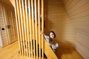 pequeño linda niña en pijama sentar en escalera en acogedor de madera minúsculo cabina casa. vida en campo. foto