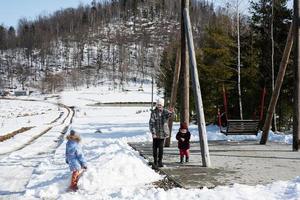 Older brother with younger sisters play near big wooden swing in forest of mountains. photo