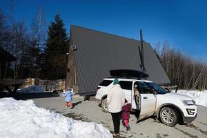 Mother and daughters against wooden triangle country tiny cabin house and suv car with roof rack in mountains. photo