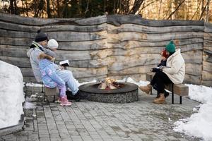 Family with three kids sitting by camp bonfire and read books on winter in forest. Children in countryside. photo