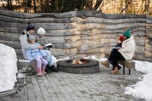 Family with three kids sitting by camp bonfire and read books on winter in forest. Children in countryside. photo