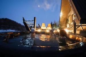 Kids enjoying bathing in wooden barrel hot tub in the terrace of the cottage. Scandinavian bathtub with a fireplace to burn wood and heat water. photo