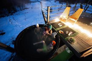 Family enjoying bathing in wooden barrel hot tub in the terrace of the cottage. Scandinavian bathtub with a fireplace to burn wood and heat water. photo