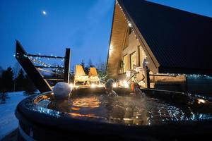 Kids enjoying bathing in wooden barrel hot tub in the terrace of the cottage. Scandinavian bathtub with a fireplace to burn wood and heat water. photo