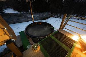 Wooden barrel hot tub in the terrace of the cottage at winter night. Scandinavian bathtub with a fireplace to burn wood and heat water. photo