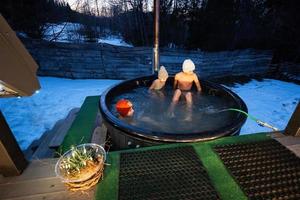 Kids enjoying bathing in wooden barrel hot tub in the terrace of the cottage. Scandinavian bathtub with a fireplace to burn wood and heat water. photo