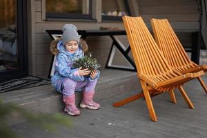 Baby girl sit on terrace off grid tiny house in the mountains and hold vase with snowdrops. photo