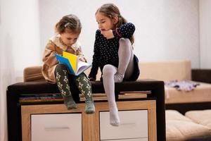 Two sisters are sitting on a couch, looking and read a book together. photo