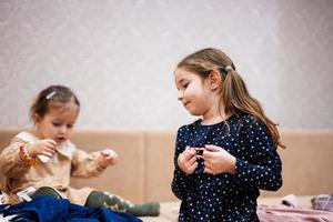 Two sisters are choosing clothes from the wardrobe at home on the sofa. Girl chooses a bracelet for her hand. photo