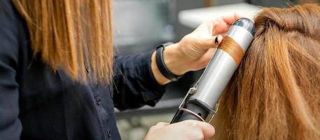 Hairdresser makes curls with curling iron photo