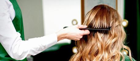 Hairdresser combing wavy hair of woman photo