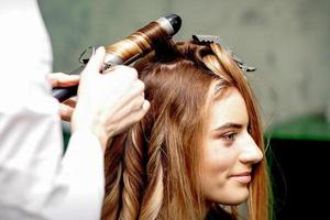 Hairdresser makes curls with curling iron photo