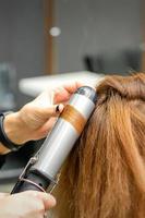 Hairdresser makes curls with curling iron photo