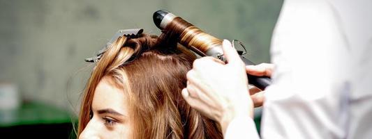 Hairdresser makes curls with curling iron photo