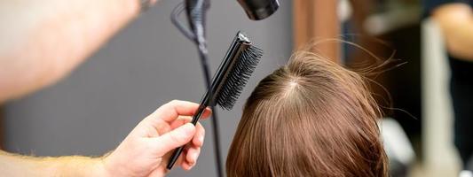 Hairdresser dries brown hair of woman photo