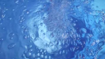 far cadere di puro blu acqua cascate su liscio puro superficie, la creazione di aria bolle, spruzzi e increspature dopo. video
