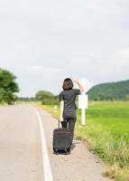 Woman with luggage hitchhiking along a road photo