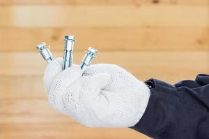 Hand in glove holding metal anchor bolt photo