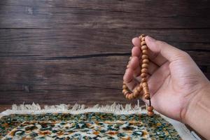 praying, palms up when praying in Islamic culture, carrying prayer beads on a prayer rug on a wooden background and there is sunshine, empty space, copy space, photo