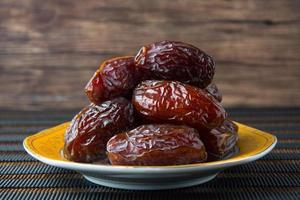 Delicious medjool dates kurma or sweet dried dates on a plate, with some falling from the plate, as a meal for breaking the fast, ramadan kareem, empty space, copy space.