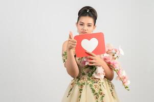 hermosa novia asiática sonriendo y posando con el signo del corazón en el fondo blanco foto