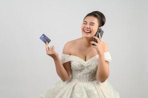 joven asiático hermosa novia destino con crédito tarjeta y teléfono inteligente en mano foto