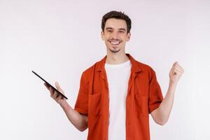 Portrait of attractive cheerful man doing winner gesture clenching fist and using device app searching web isolated over white color background photo
