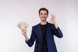 retrato de un hombre alegre que muestra el signo de ok y tiene dinero sobre fondo blanco foto