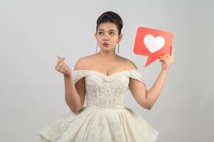 Asian beautiful bride smiling and posing with heart sign on white background photo