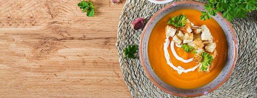 Pumpkin soup in a bowl served with parsley and croutons. Vegan soup. Thanksgiving day food. Halloween meal. Banner. Top view photo
