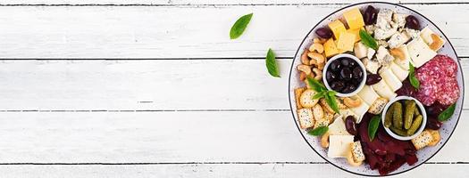 Antipasto platter with basturma, salami, blue cheese, nuts, pickles and olives on a white wooden background. Banner. Top view, overhead photo