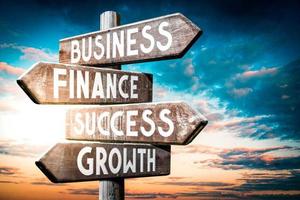 Business, Finance, Success, Growth - Wooden Signpost with Four Arrows, Sunset Sky in Background photo
