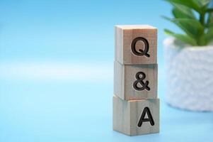 Q and A text engraved on wooden blocks with light blue and table plant background. Question and answer concept. Copy space photo