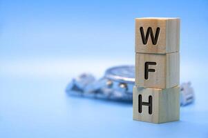 WFH text represent work from home text engraved on wooden blocks with light blue and watch background. Work from home concept. Copy space photo