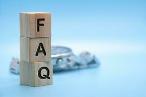 FAQ text engraved on wooden blocks with light blue and watch background. Question and answer concept. Copy space photo