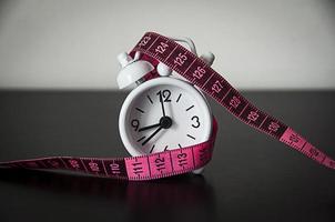 White alarm clock wrapped with measuring tape background. photo