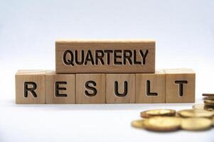 Quarterly result text engraved on wooden blocks with golden coins background. Business result concept photo