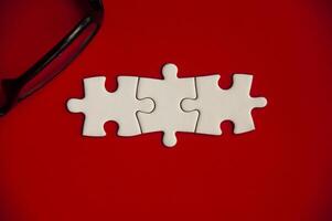 Top view of jigsaw puzzle pieces with glasses on red cover background. Copy space photo