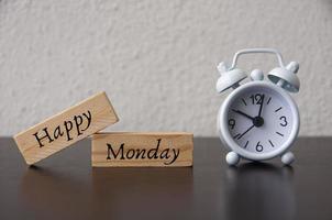 Happy Monday text on wooden blocks with white alarm clock background. photo