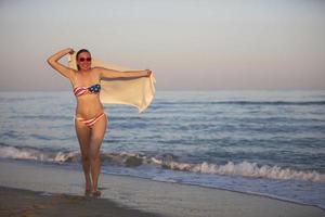 A middle-aged woman in a swimsuit with an American flag print walks along the seashore. photo