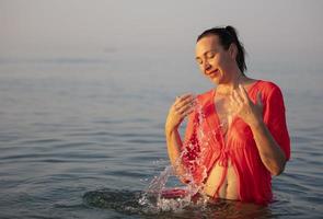 hermosa mayor mujer se baña en el mar y salpicaduras agua. foto