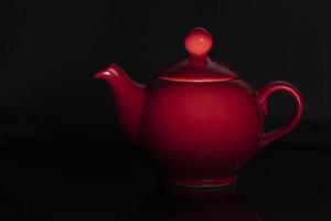 Teapot of red color of the classical form on a black background. photo