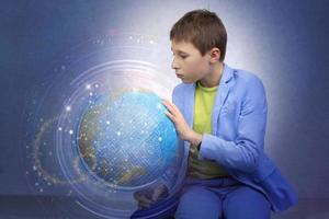 On a blue abstract background, a boy in a suit examines and studies the globe of the planet Earth. Research and teaching. photo