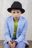 A sad stylish boy in an elegant hat and a blue suit is thoughtful. photo