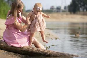 un hermosa madre es caminando con su pequeño hija por el río. maternidad. foto