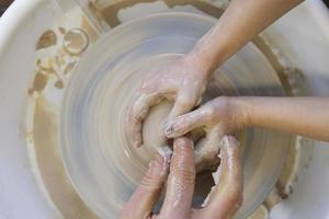 Close-up of a potter's hands and a child's hand with an item on a potter's wheel. Working with clay. Clay workshop. Craft training. photo