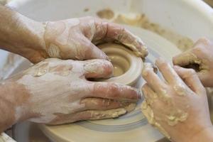 The potter teaches the craft to the child. Close-up of a potter's hands and a child's hand with a product on a potter's wheel. Working with clay. Clay master class. photo