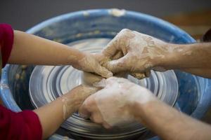 The potter teaches the craft to the child. Close-up of a potter's hands and a child's hand with a product on a potter's wheel. Working with clay. Clay master class. photo