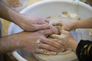 The potter teaches the craft to the child. Close-up of a potter's hands and a child's hand with a product on a potter's wheel. Working with clay. Clay master class. photo